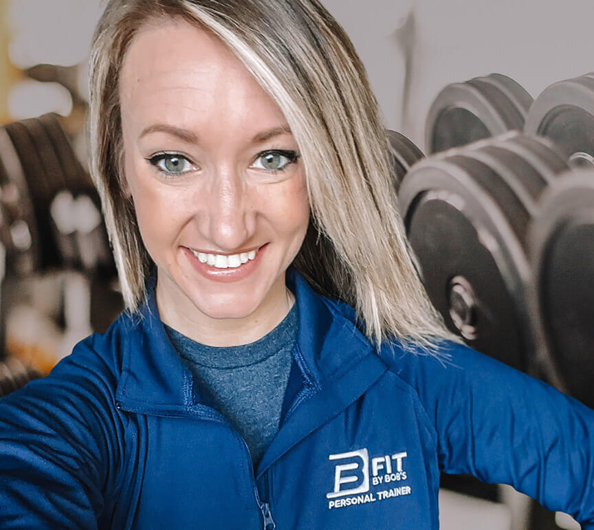 Smiling personal trainer in gym with dumbbells.